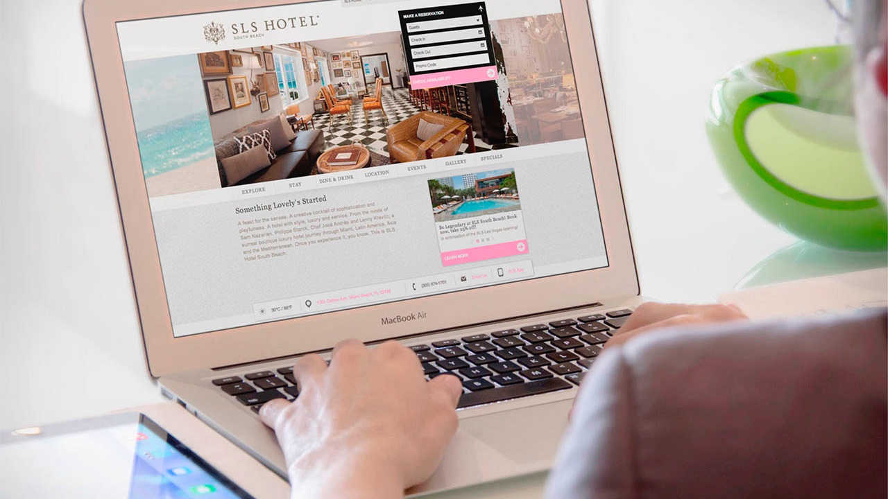 A woman is using a laptop to design a SLS Hotels website.