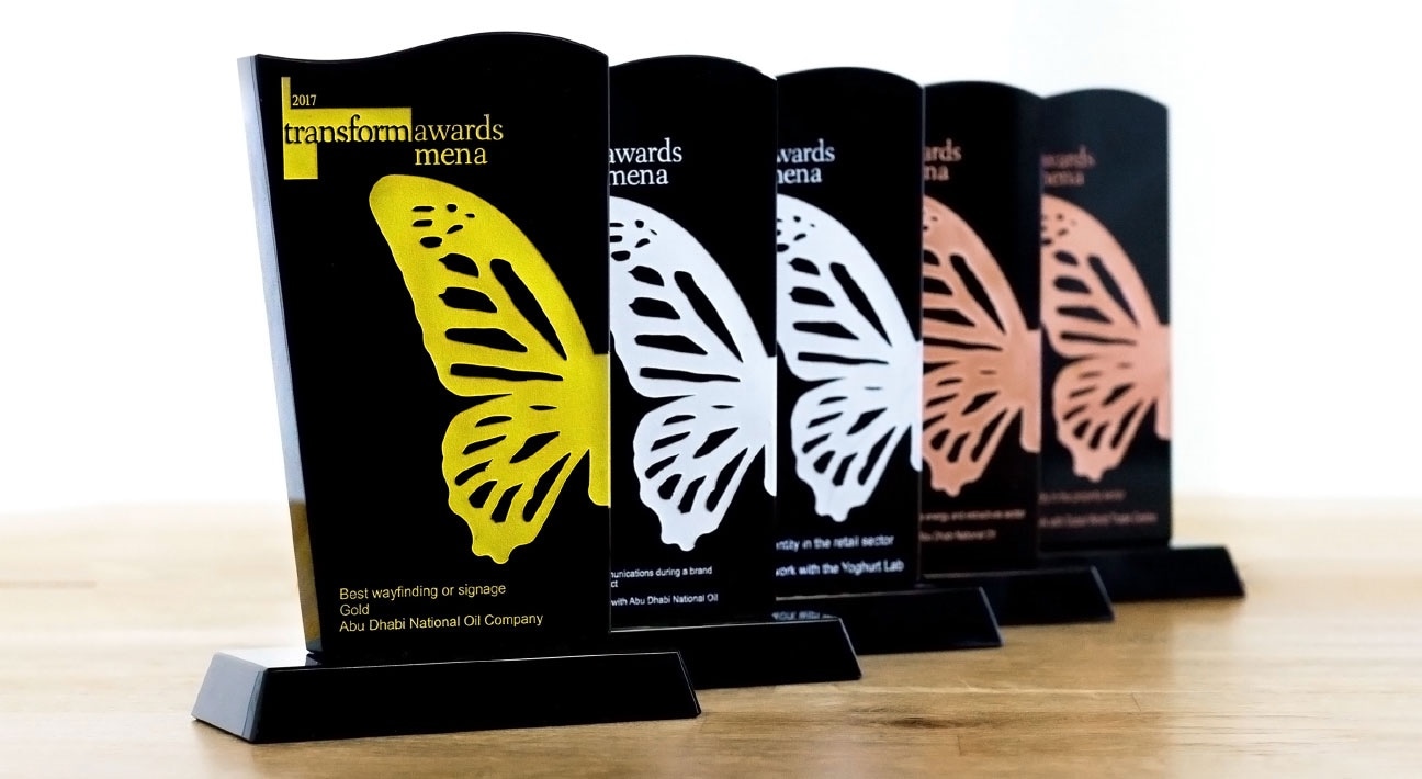 Five butterfly shaped awards on a wooden table.