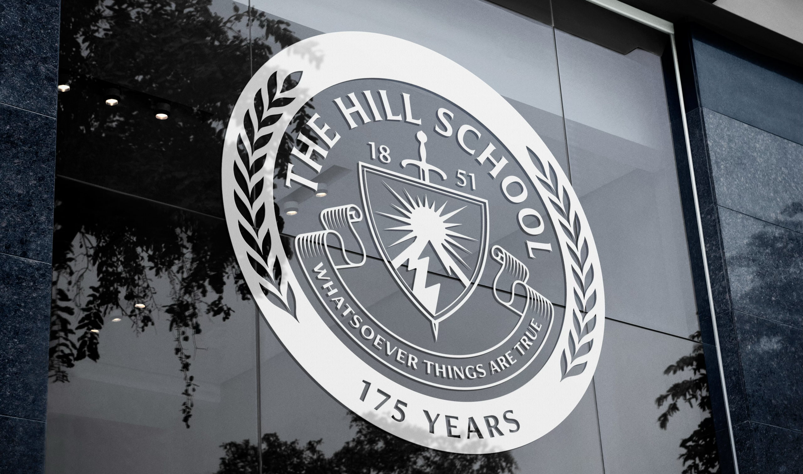 The Hill School emblem on glass, featuring the motto "Whatsoever Things Are True," the year 1851, and "175 Years" within a laurel wreath border, reflects a revitalized identity.