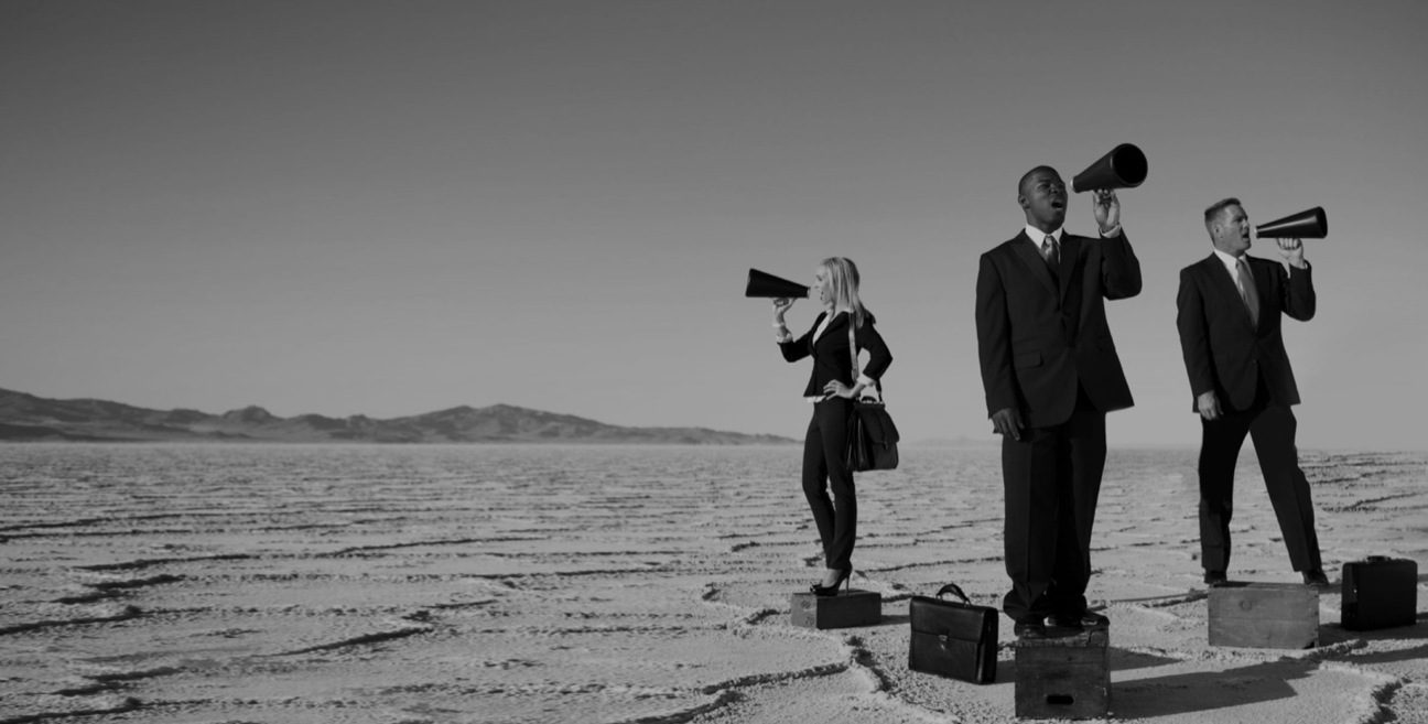 Three business people standing in the desert with megaphones.