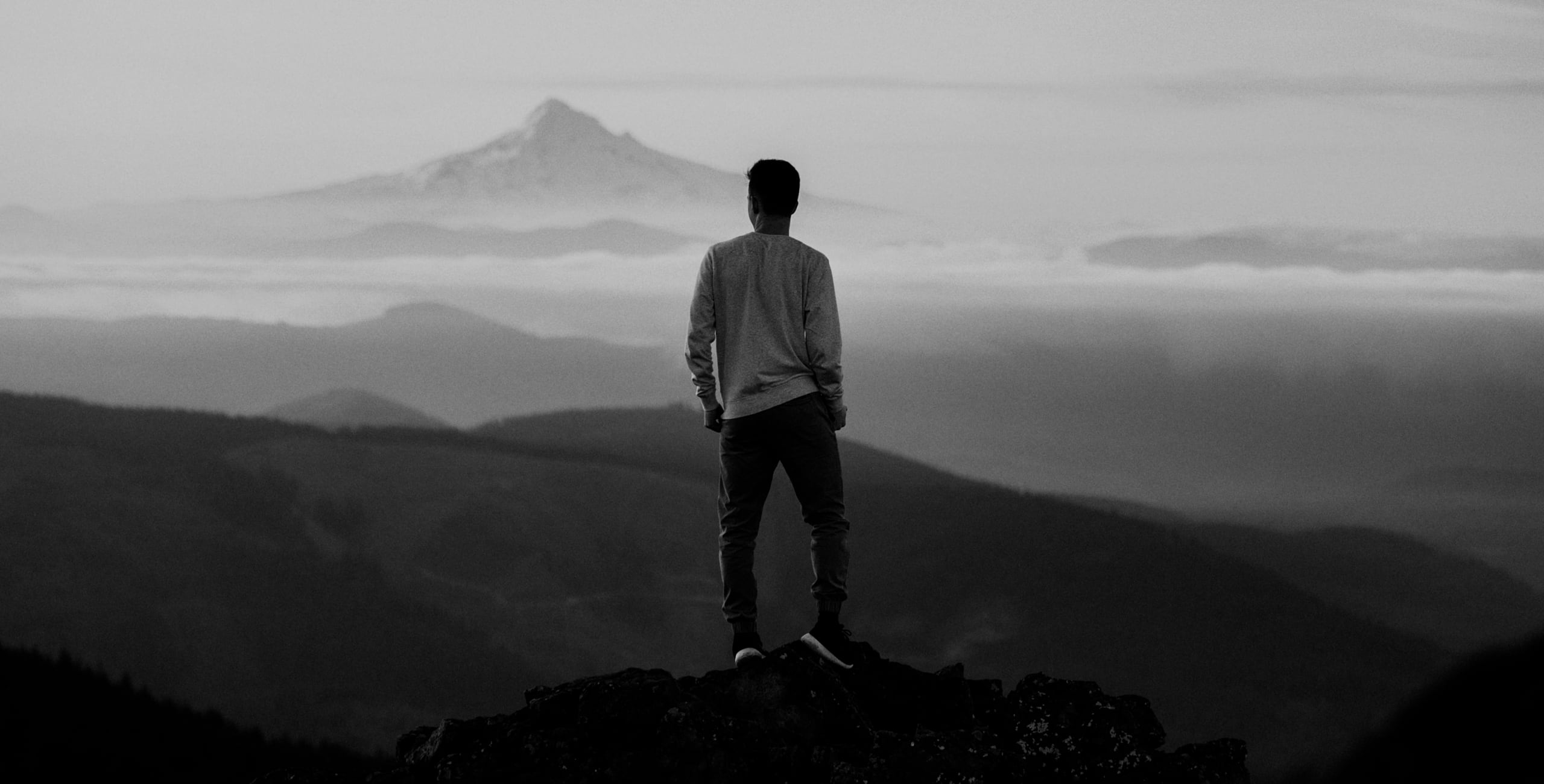 A man standing on top of a mountain with mountains in the background.