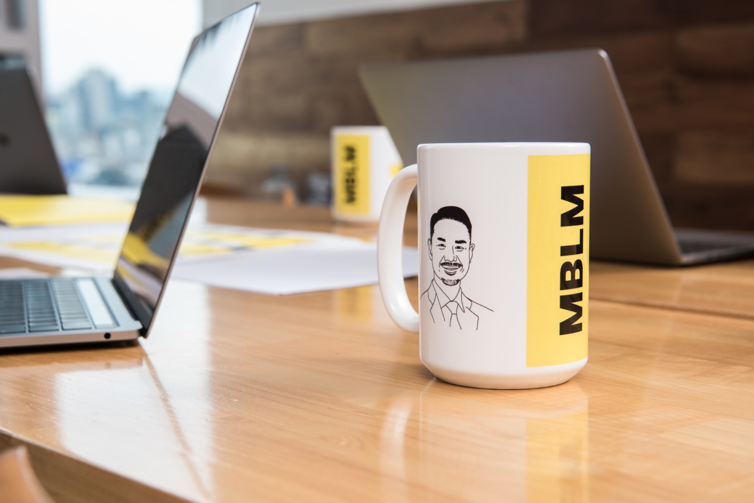 A coffee mug with the word mblm on it sits on a desk.