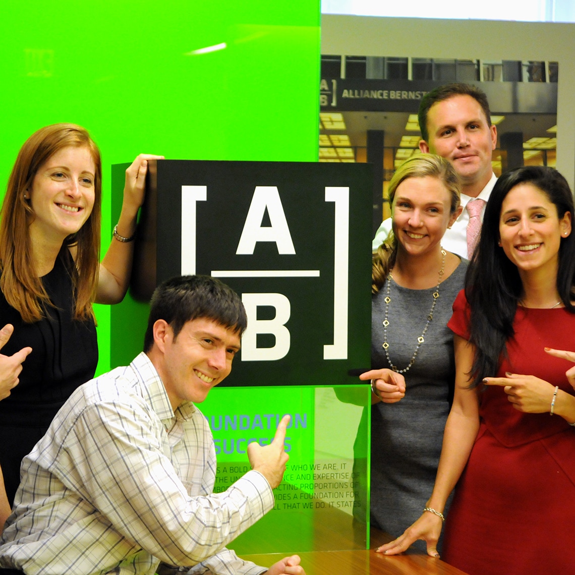 employees taking a photo at the brand's launch event, pointing to the new logo developed for AB (AllianceBernstein)