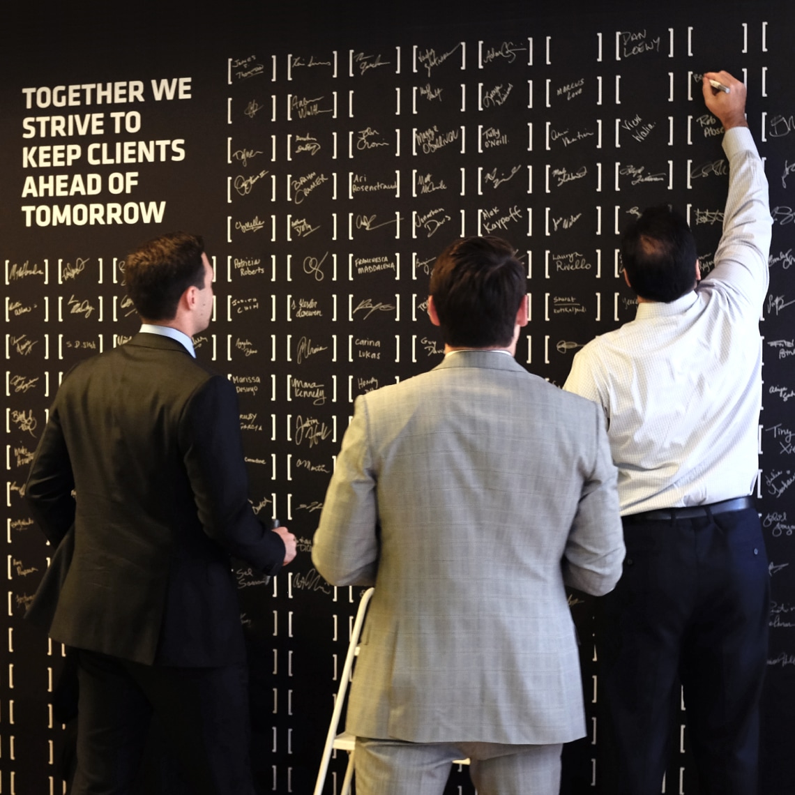 Three employees write their names on a wall, showing their connection to the new brand.
