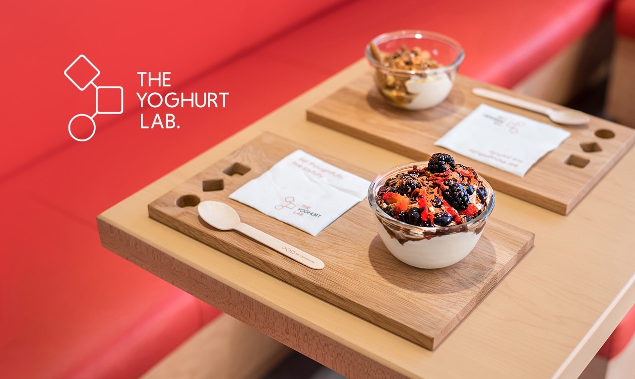 a table with two dishes of yogurt and fruits and the logo of the The Yoghurt Lab