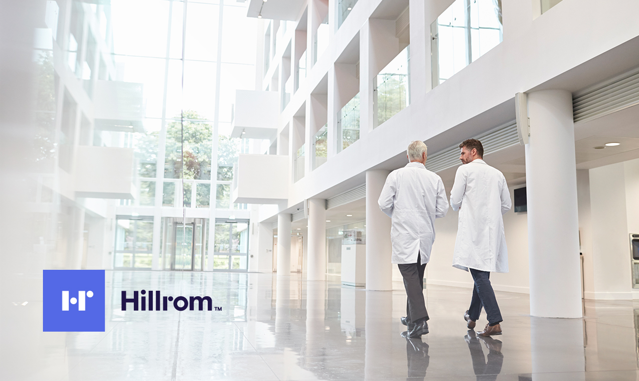 two men in lab coats walking through a building and the logo of Hillrom