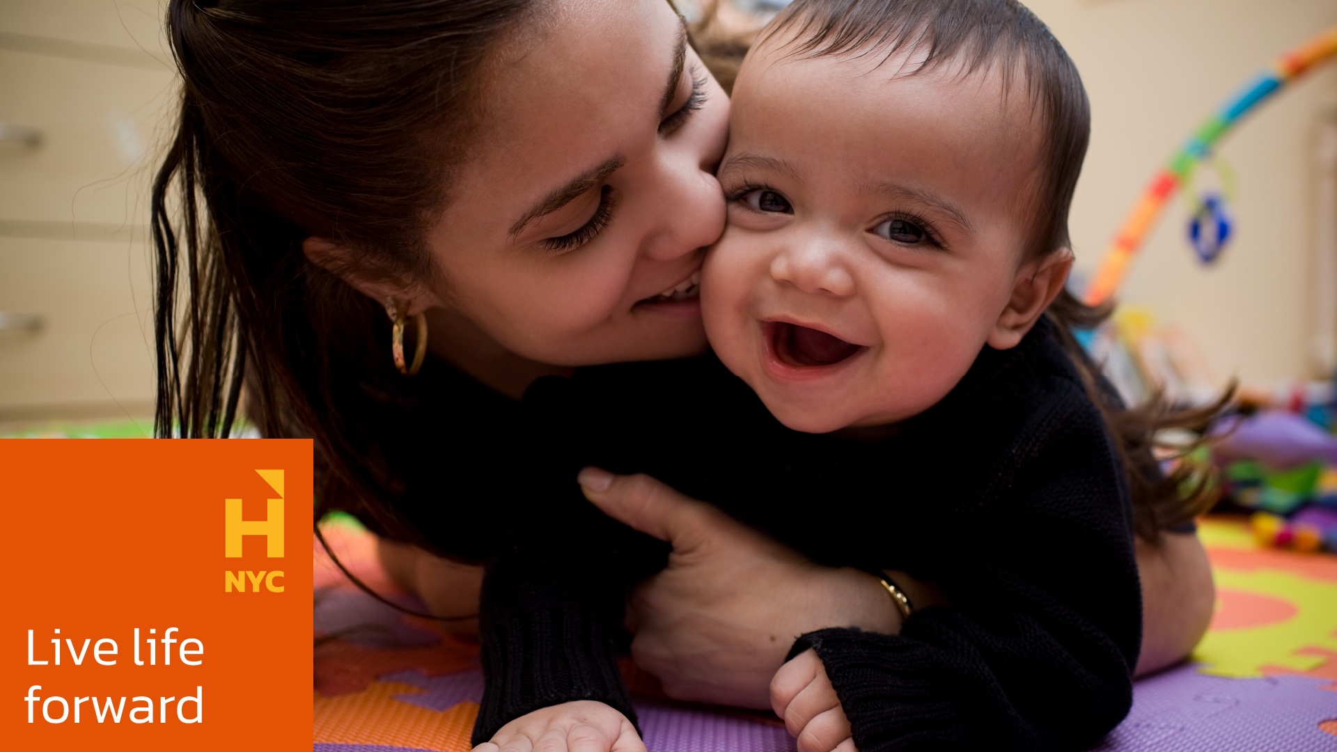 A young woman with a smiling baby in her arms, with the new branding system developed for West End Residences, applied in the lower left corner.