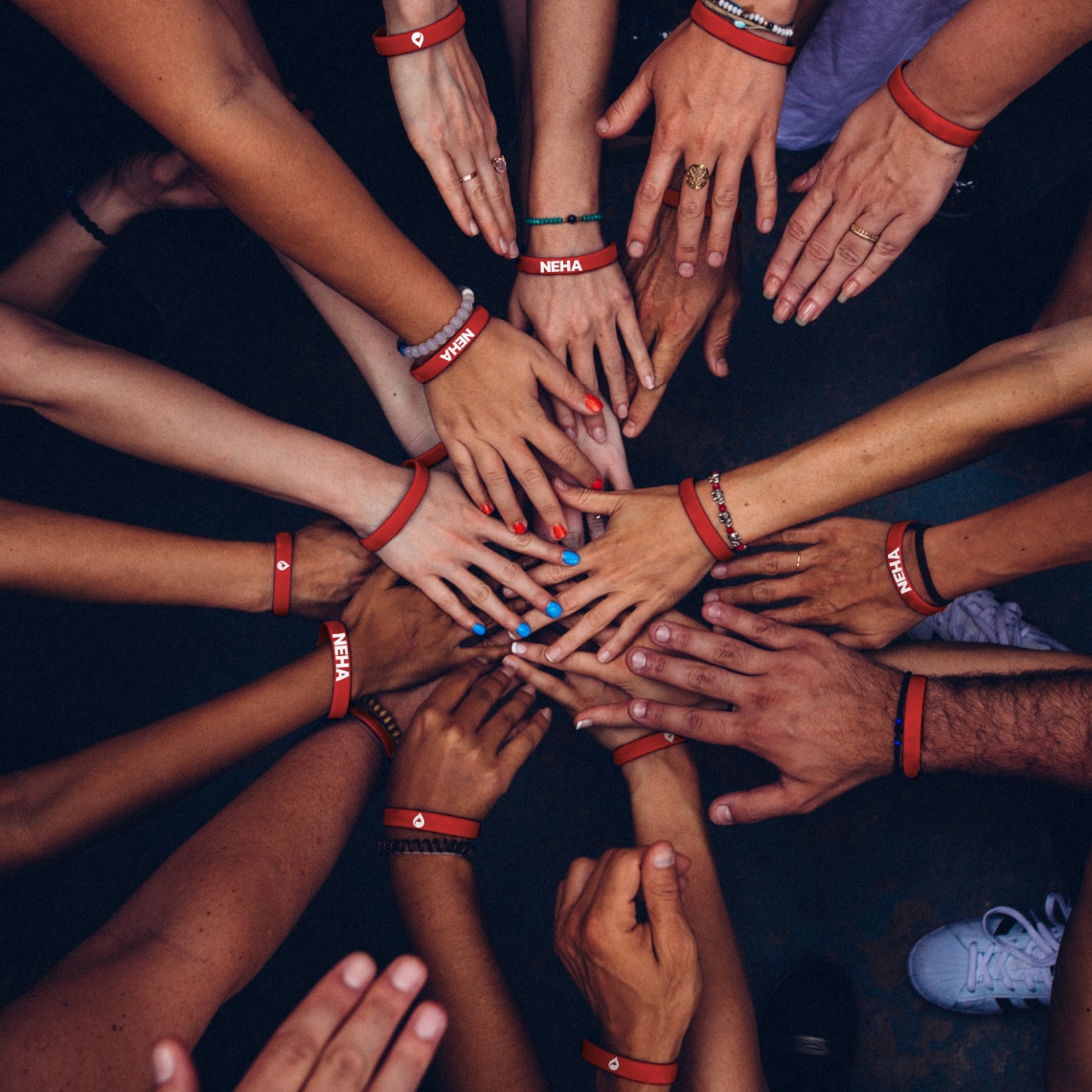 a group of people wearing red bracelets with the NEHA logo, putting their hands together