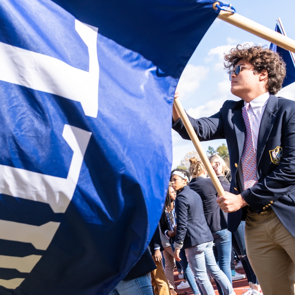 a teenage student holding a flag with part of the logo of the Hill School
