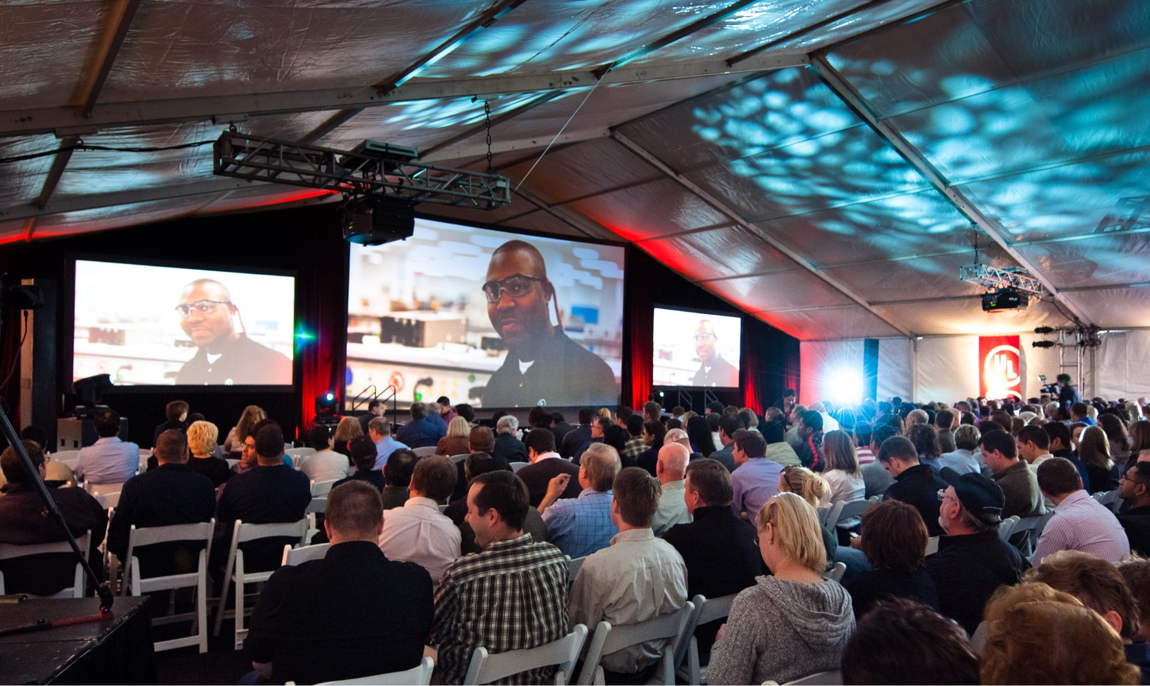 a group of people look at three large screens displaying the unveiling of the brand's launching campaign.