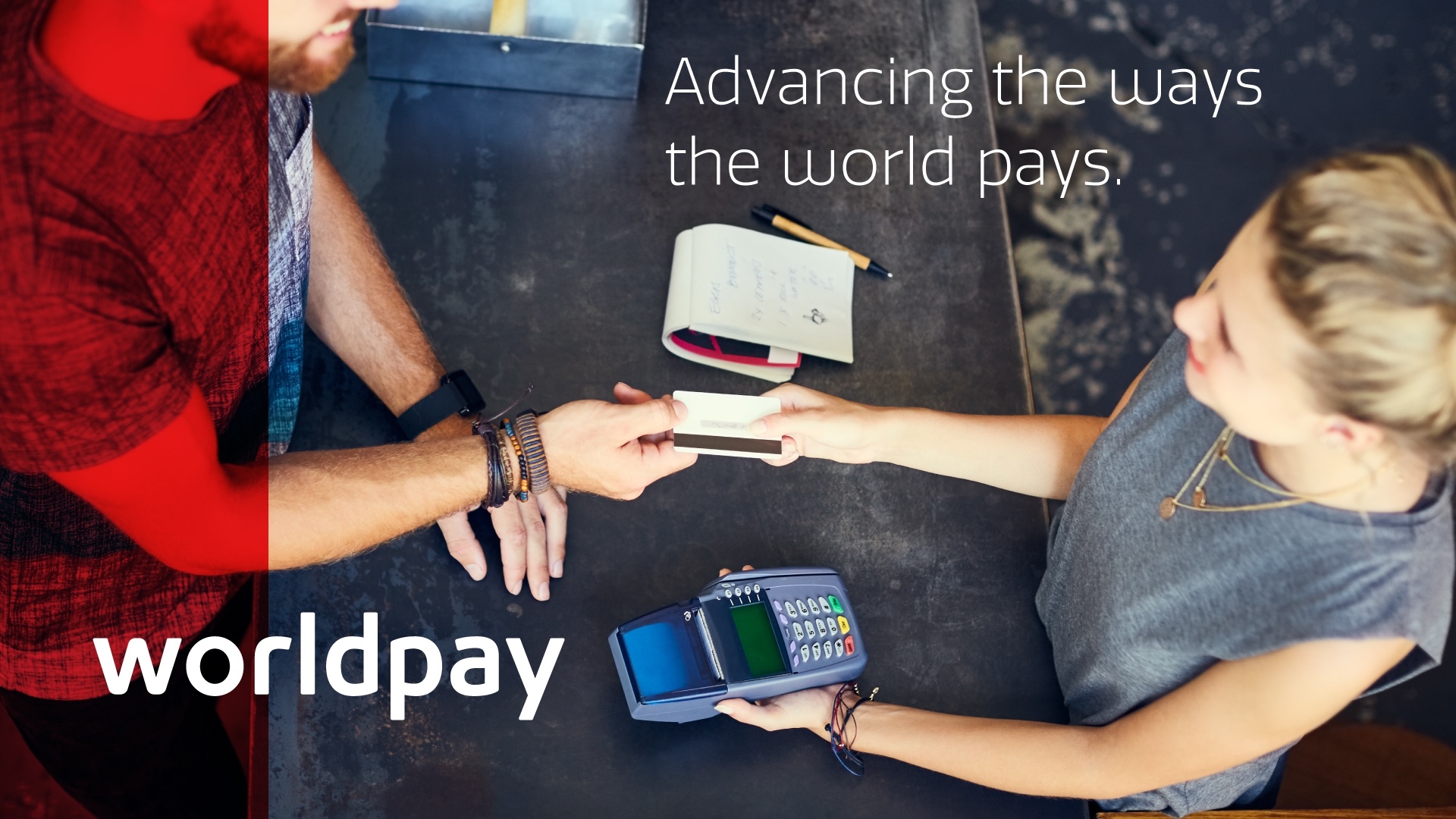 a man handing a credit card to a woman with a pos in hand, with the worldpay logo on it.
