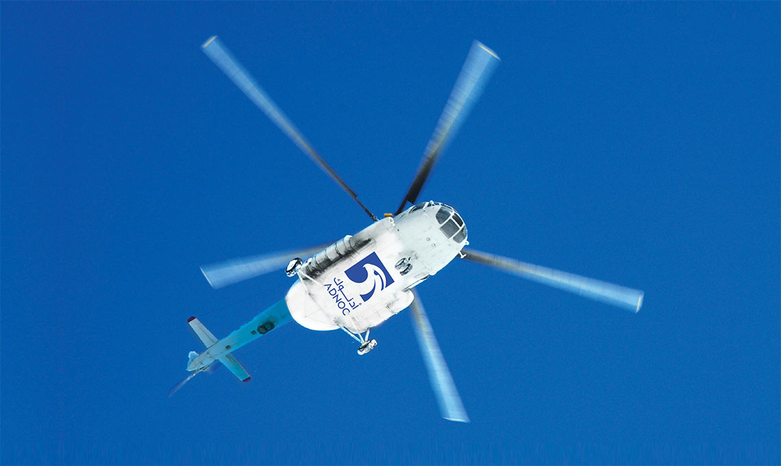 a helicopter with the ADNOC logo at the bottom, flying through a blue sky with propellers.