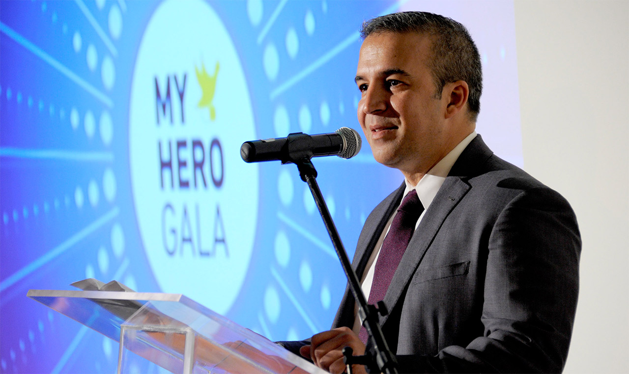 A man in a suit standing at a podium at the My Hero Gala.