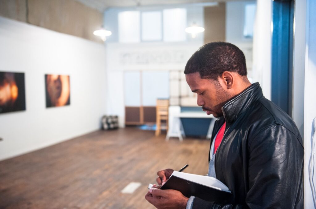 A man writing in a notebook in an art gallery.