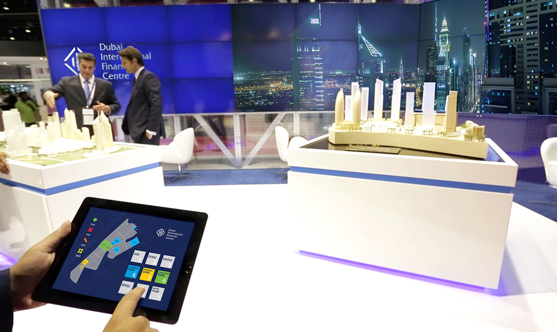 A man is holding an ipad while looking at a model of a city.