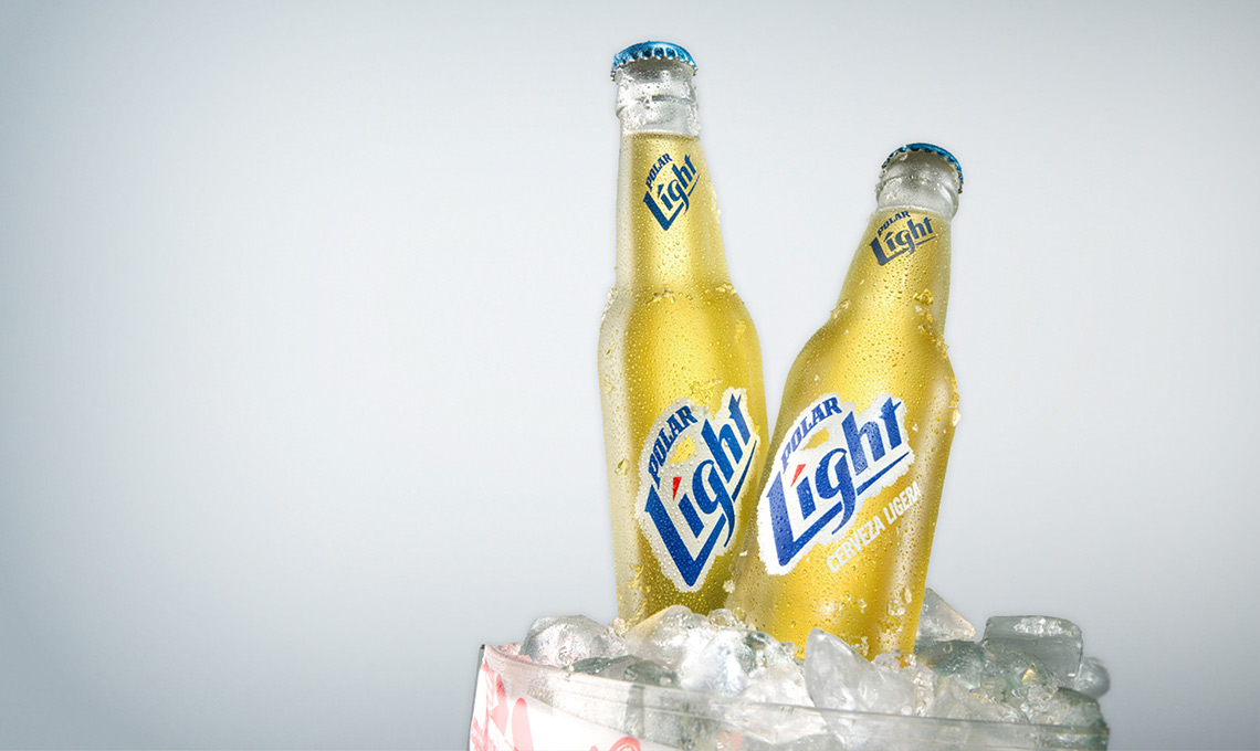Two bottles of Cervecería Polar beer sitting on top of ice.