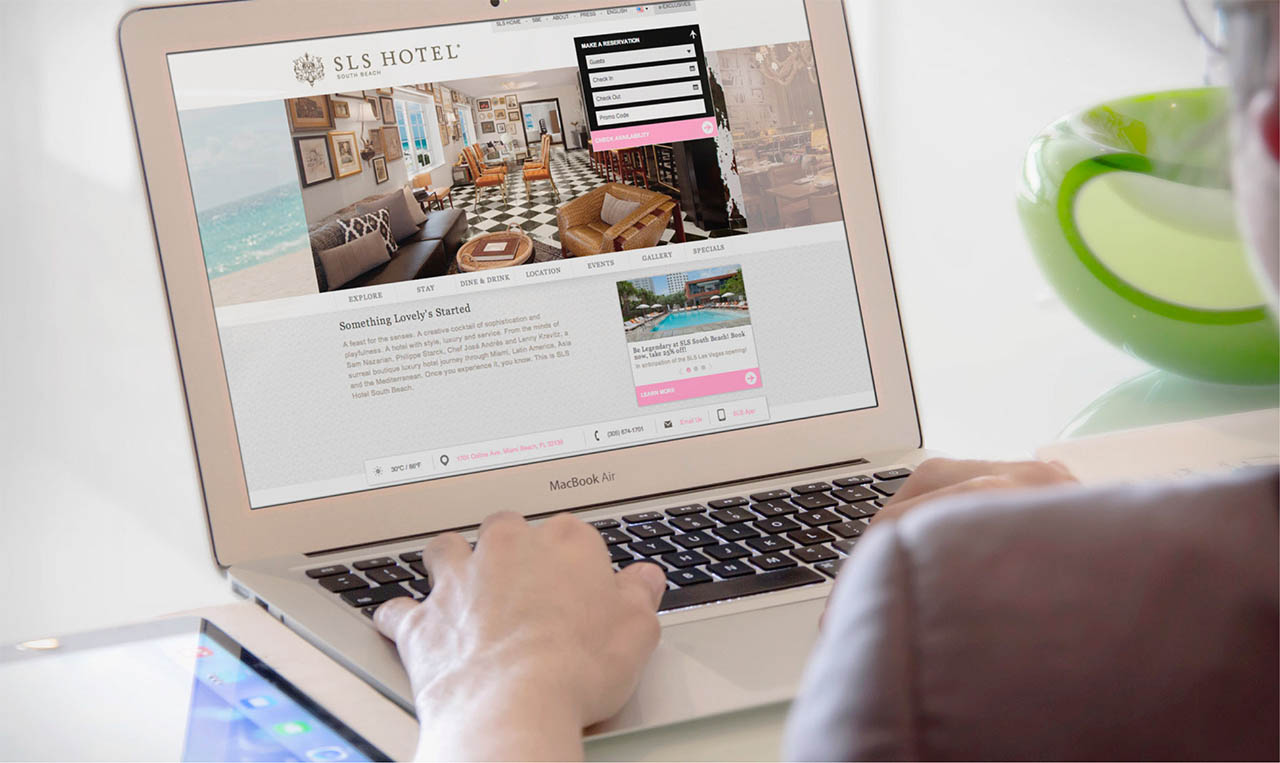 A woman is using a laptop to design a website for SLS Hotels.