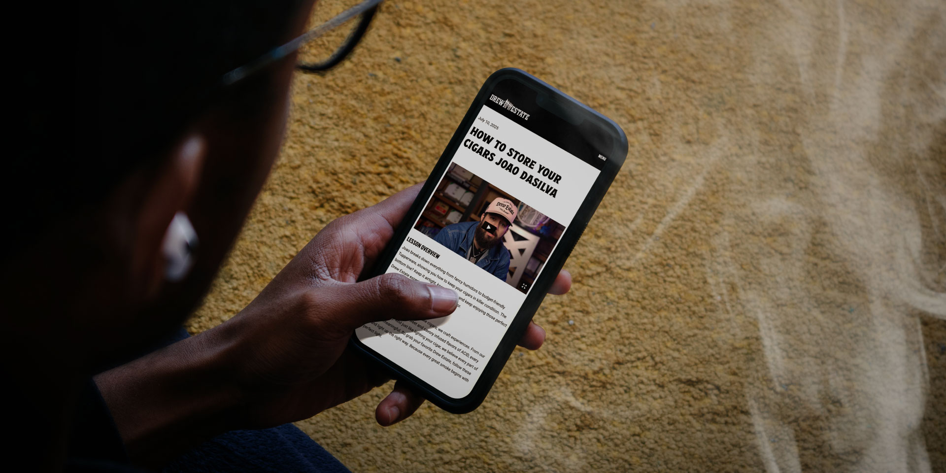 A person holds a smartphone displaying an article titled "How to Store Your Cheap 30-80 Zausa" with a photo of a man and text on the screen.