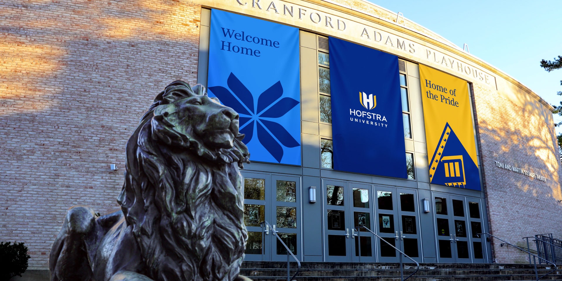 A bronze lion statue stands in front of the Cranford Adams Playhouse, with banners displaying "Welcome Home" and "Hofstra University" hanging above the entrance.