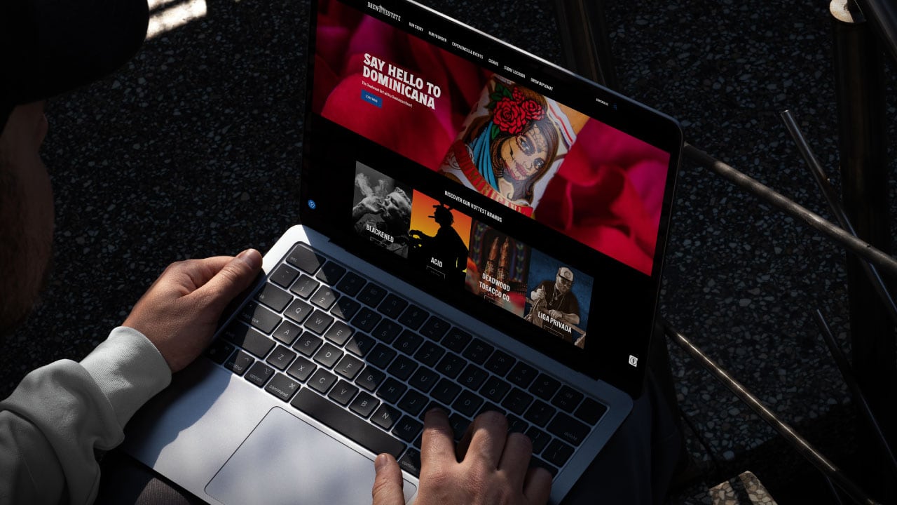 Person using a laptop outdoors, viewing a website with "SAY HELLO TO DOMINICANA" and images of travel destinations on the screen.