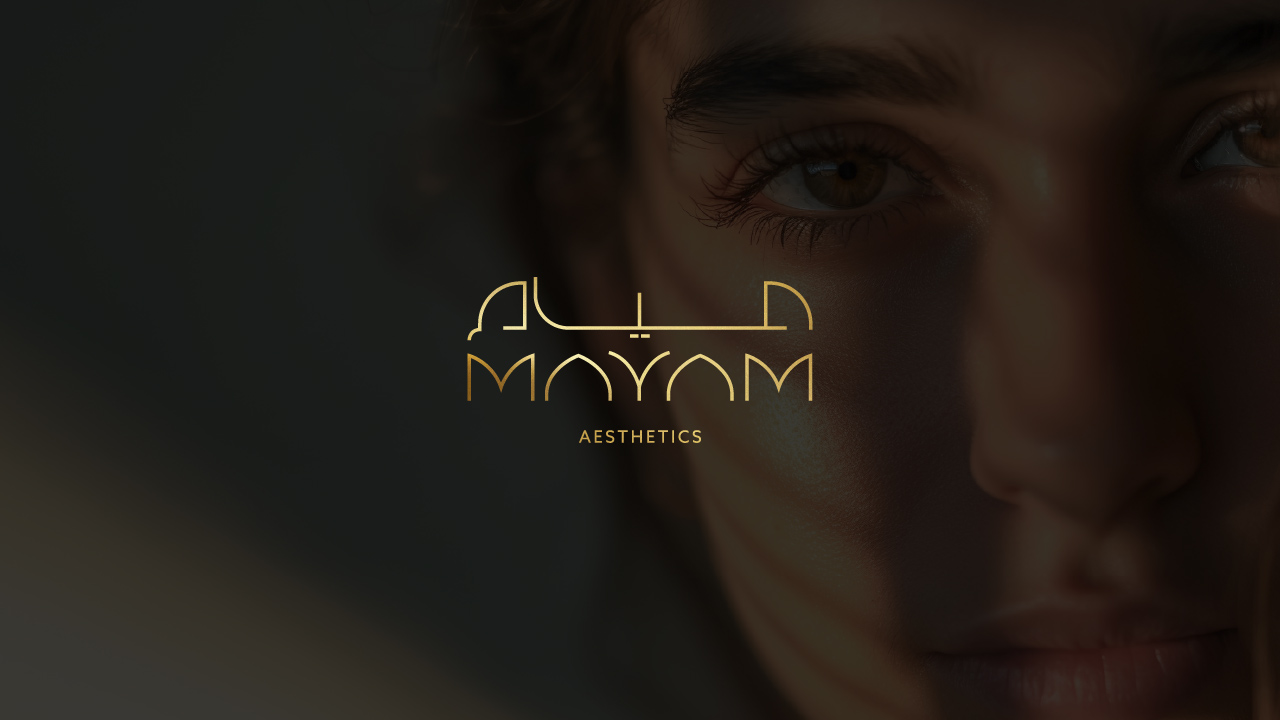 Female Middle-eastern youth facing the camera, behind a black overlay with reduced opacity and a gold-gradient Mayam Aesthetics logo.