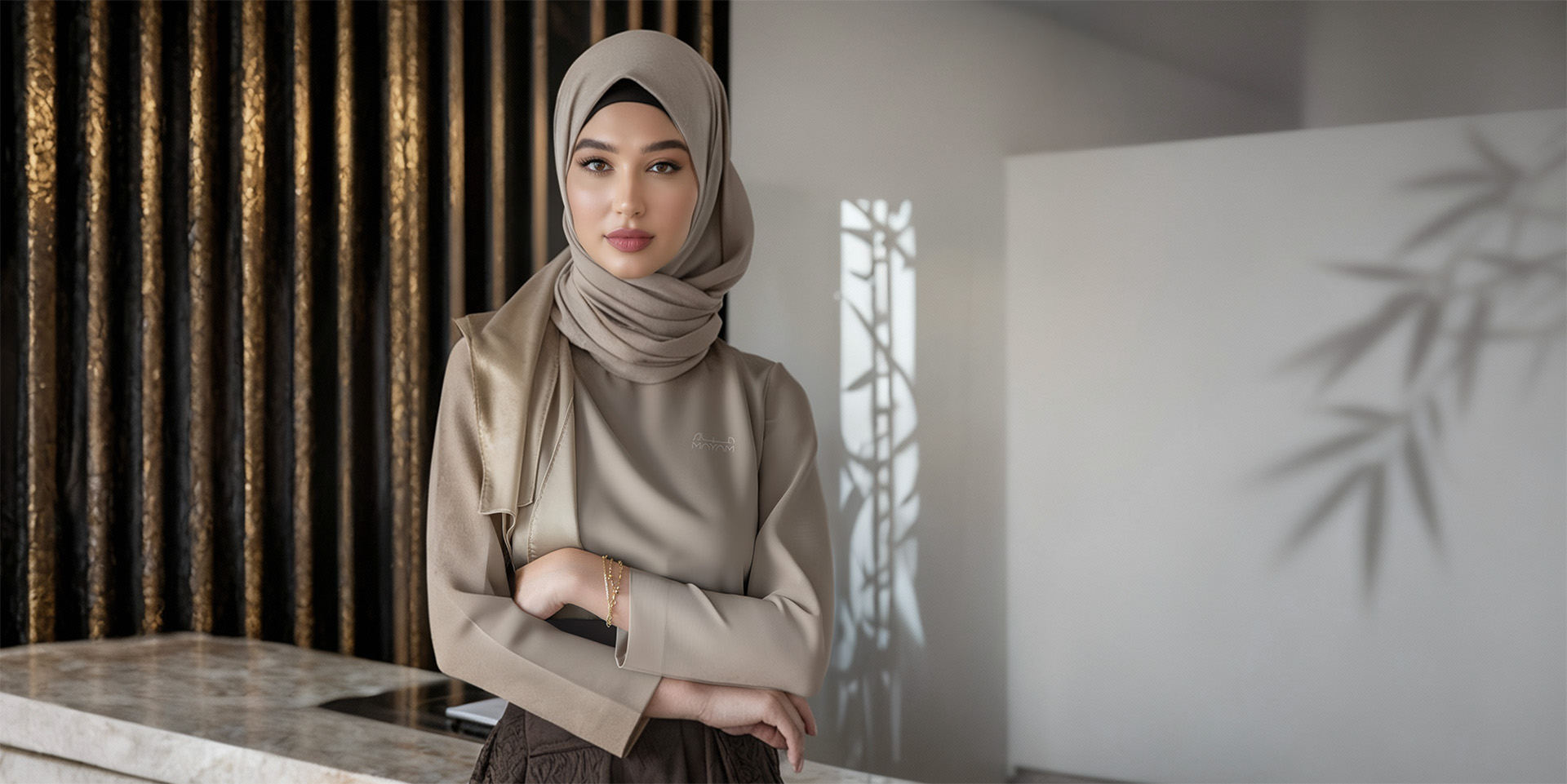 An Arab women serving as a Mayam employee, in light Mayam branded uniform, standing cross-armed in a Mayam branded environment.