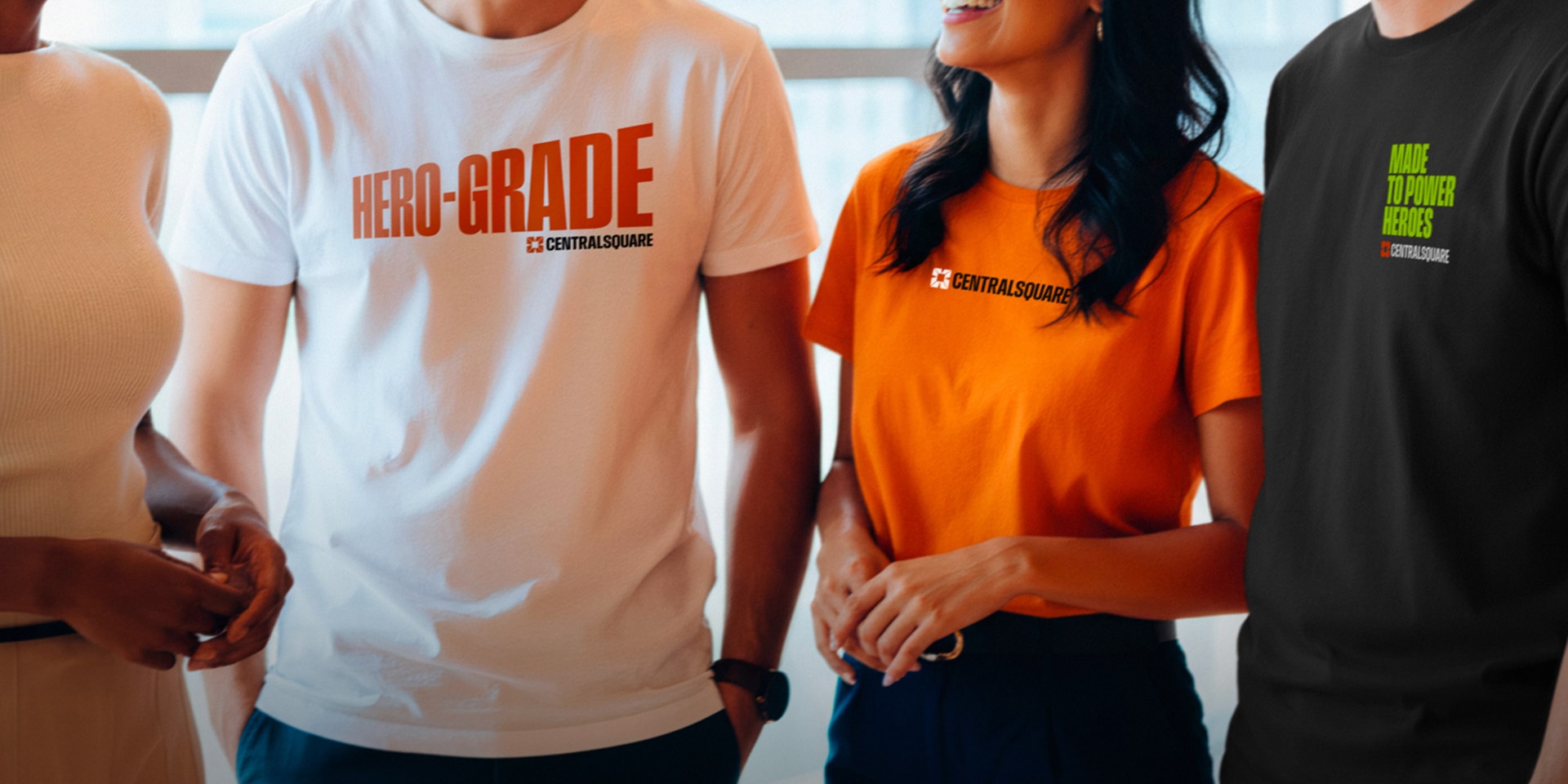 Four people standing together, wearing branded t-shirts with CentralSquare logos and different slogans, in a bright indoor setting.