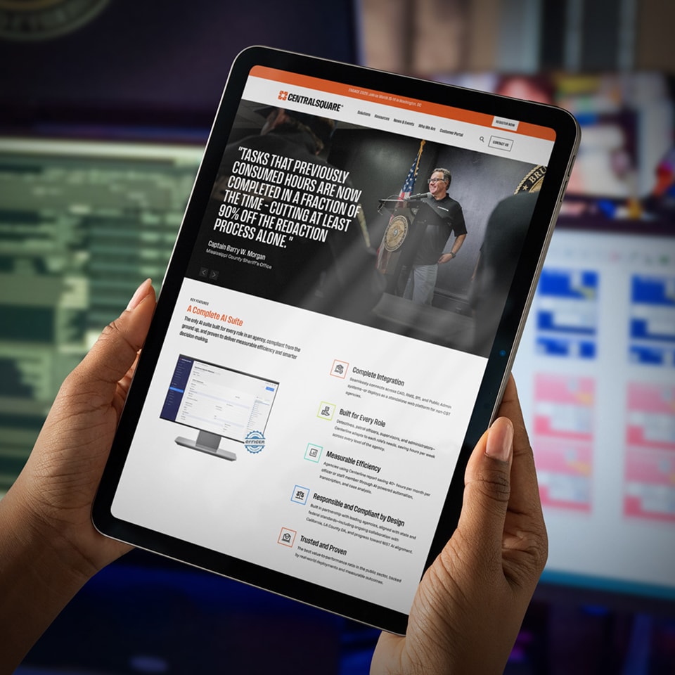 A person holds a tablet displaying a CentralSquare website page featuring government software solutions and a testimonial from a uniformed official.