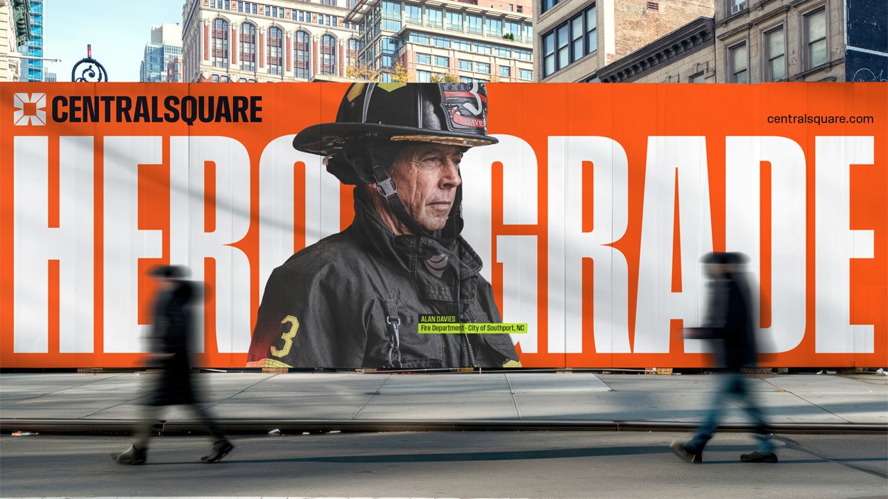 Large billboard with the image of a firefighter and the words “HERO GRADE” in bold text, located on a city sidewalk as people walk past.