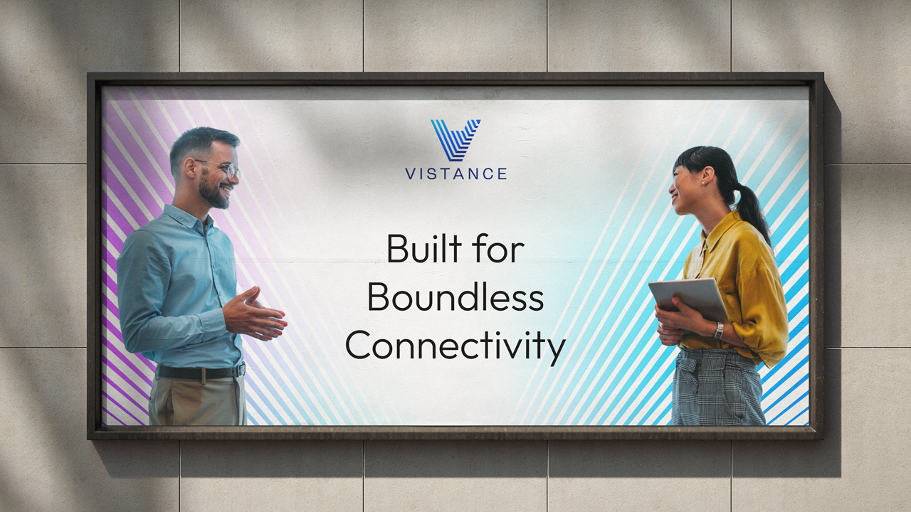 Two people standing and talking in front of a billboard displaying the Vistance logo and the text, "Built for Boundless Connectivity.