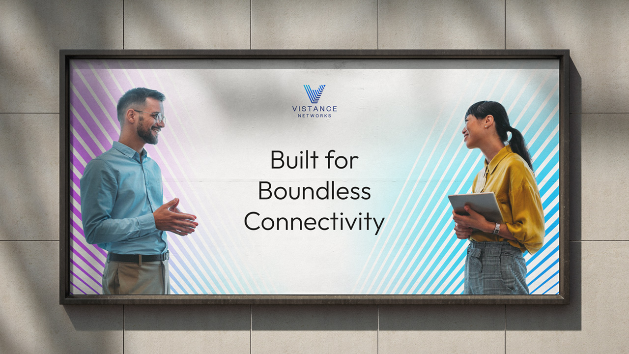 A man and a woman stand facing each other and smiling next to the text “Built for Boundless Connectivity” on a Vistance Networks billboard.
