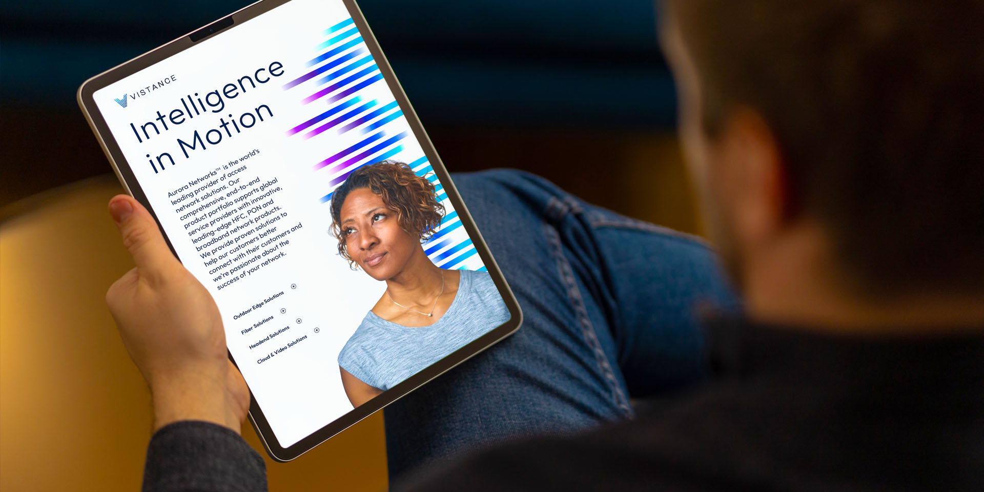 A person holding a tablet displaying an article titled "Intelligence in Motion" with a portrait of a woman and colorful graphic elements on the screen.