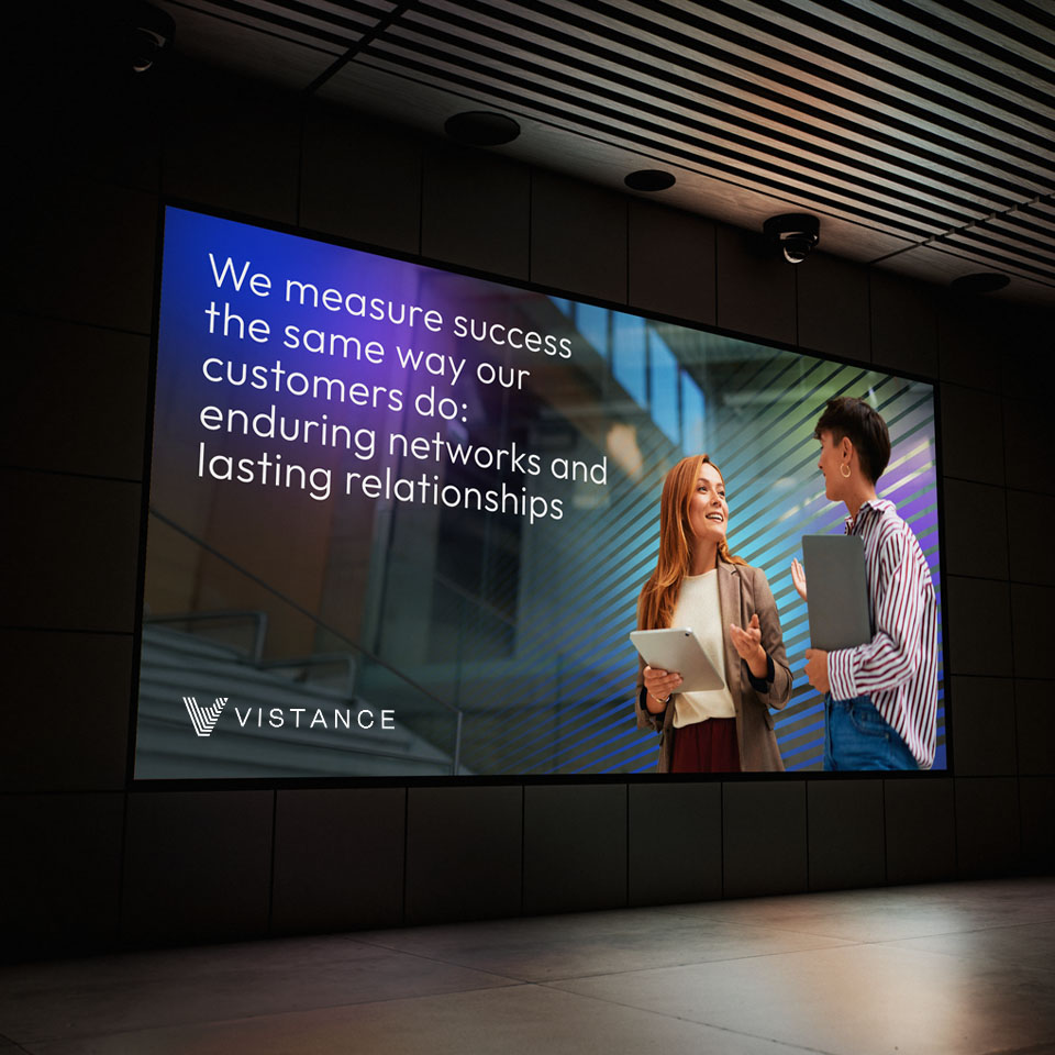 A large digital billboard shows two people talking and smiling, with the Vistance logo and a message about measuring success through networks and relationships.