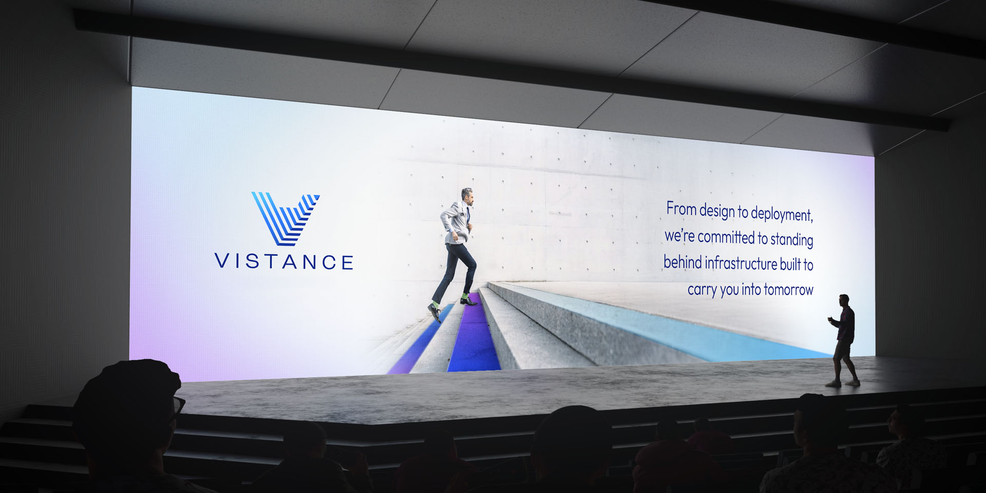 A presenter stands on stage in front of a large screen displaying the Vistance logo, a person ascending steps, and text about infrastructure commitment.