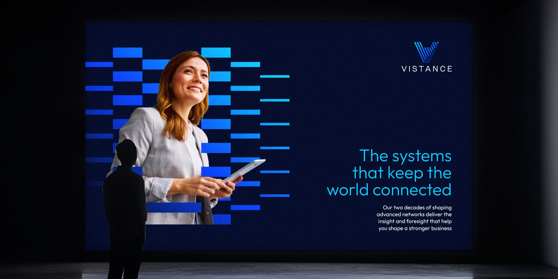 A person stands viewing a large digital display featuring a smiling woman with a tablet, the Vistance logo, and the text: "The systems that keep the world connected.