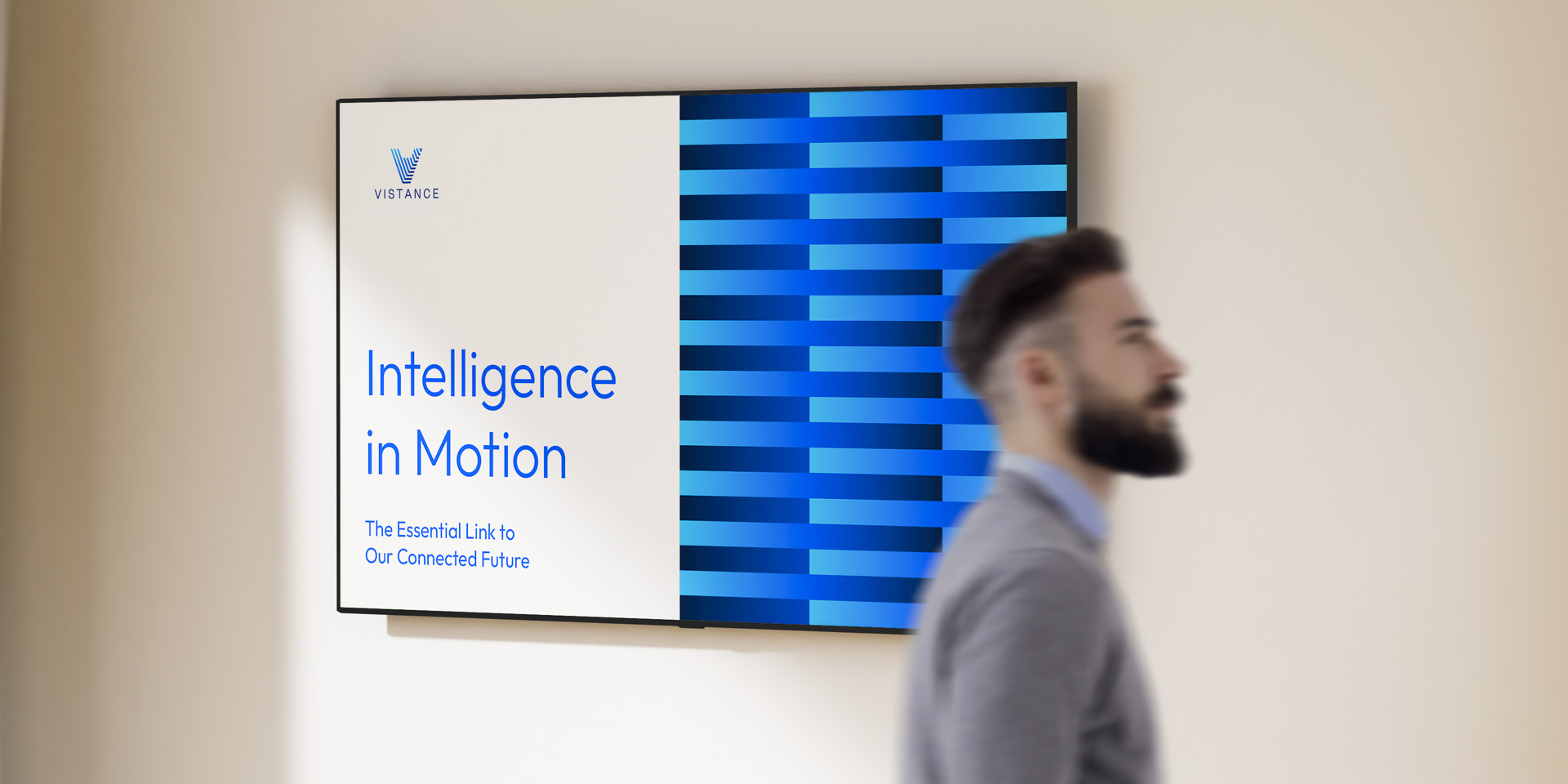 A man walks past a wall-mounted screen displaying “Intelligence in Motion” and a blue striped pattern, with the Vistance logo in the top left corner.
