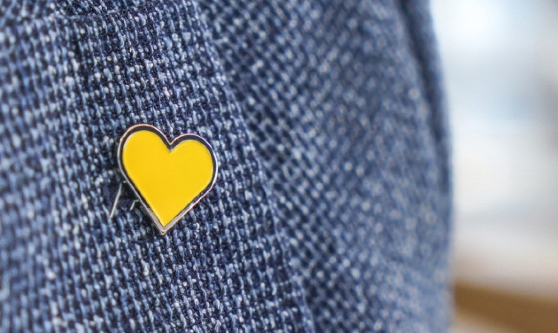 A yellow heart-shaped pin is attached to a textured blue fabric.