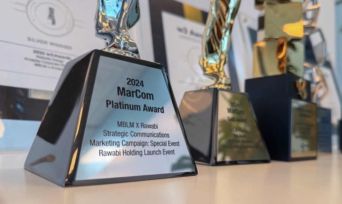 Close-up of a 2024 MarCom Platinum Award trophy for Strategic Communications, with other trophies blurred in the background.