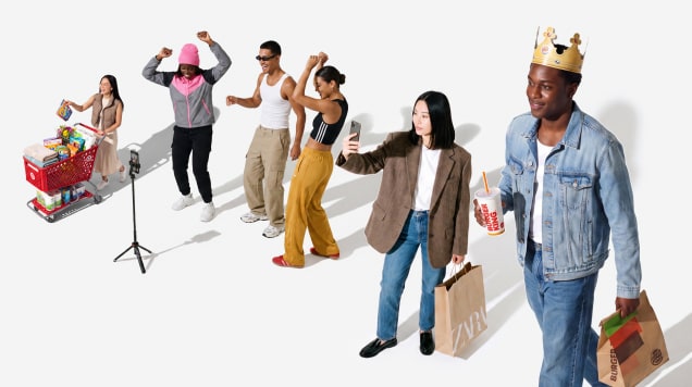 A diverse group of people pose with shopping bags, food, and a grocery cart in front of a white background, some engaging with a smartphone and video camera.