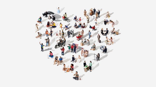A diverse group of people is arranged in the shape of a heart on a white background, representing community and inclusivity.