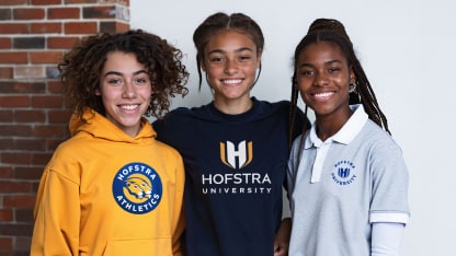 Three young people stand side by side, smiling. They wear Hofstra University and Hofstra Athletics shirts, with a brick wall and white background behind them.