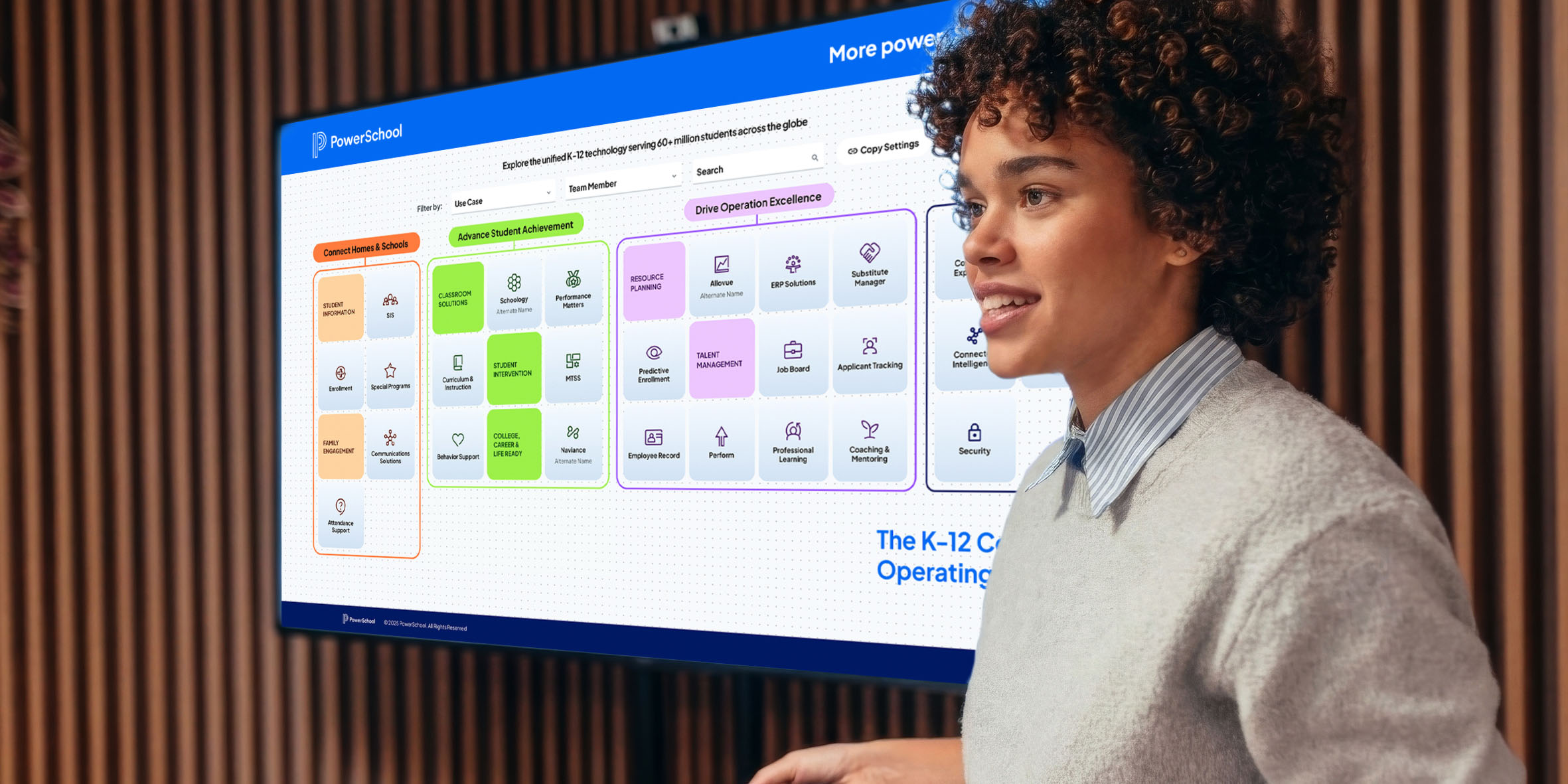 A woman presents beside a large screen showing PowerSchool’s K-12 platform, with color-coded modules for school operations.